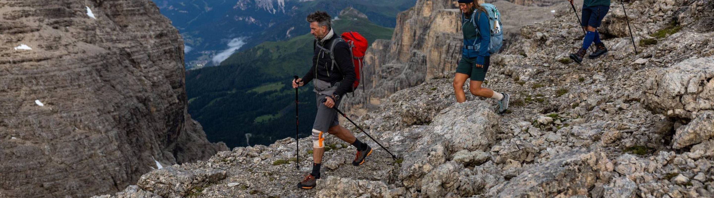 people hiking down a rocky slope in the mountains. The man in front is wearing Bauerfeind's Outdoor Knee Support, which can help relieve knee pain.