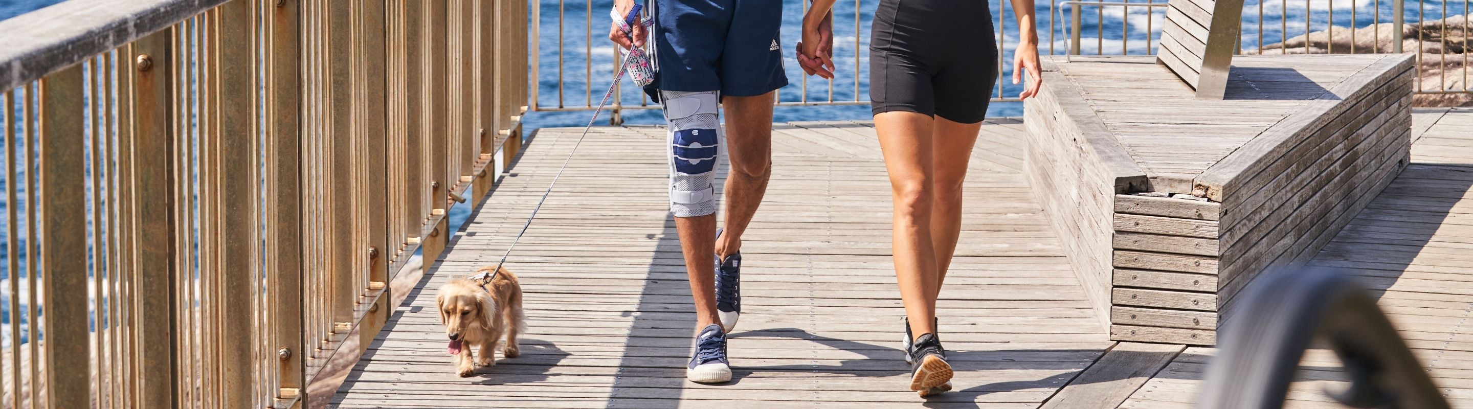 couple walking on the beach. One is wearing Bauerfeind's GenuTrain S Knee Brace