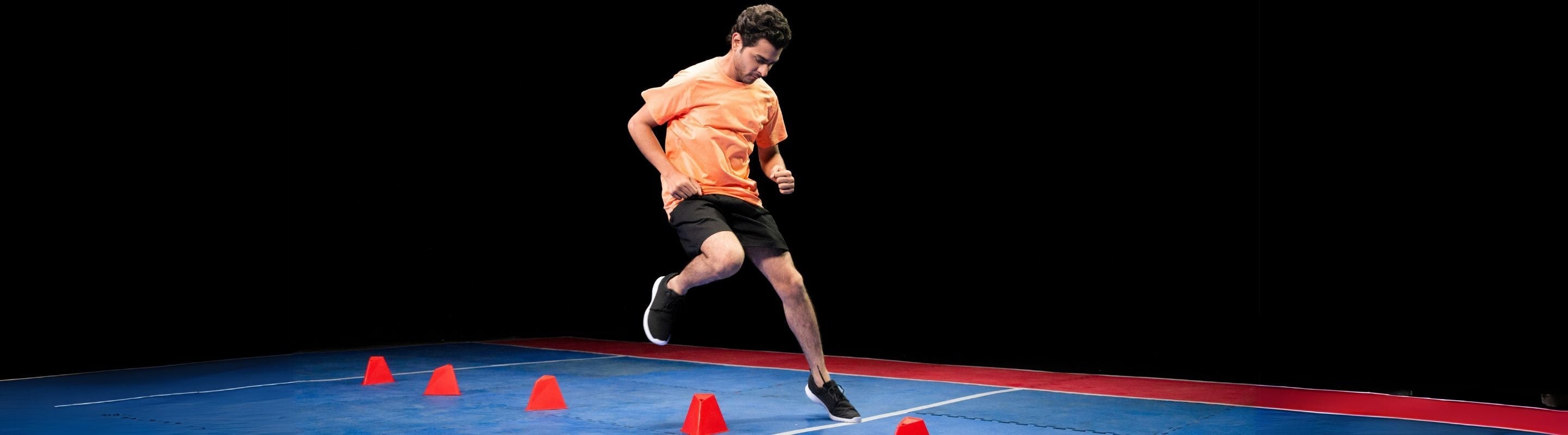 man agility training with lateral step overs. He is jumping over a serious of cones and wearing an orange shirt