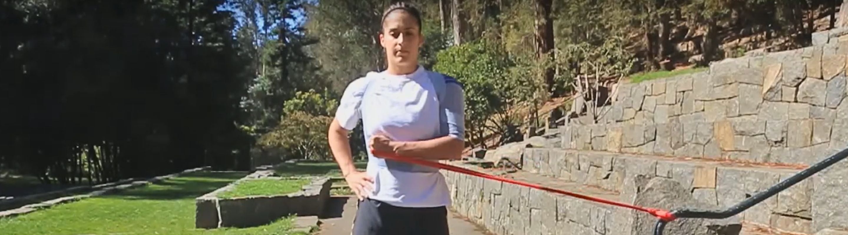 Woman doing internal shoulder rotations at the park. She is wearing Bauerfeind's OmoTrain Shoulder Support