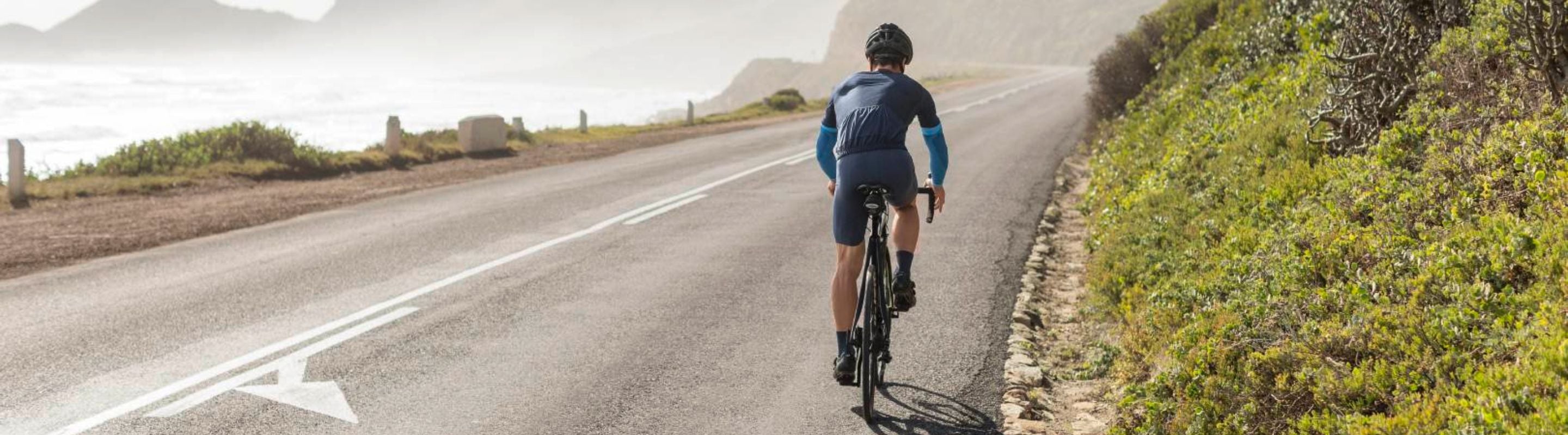 Man cycling on a road near the ocean. He's wearing Bauerfeind Arm Compression Sleeves.