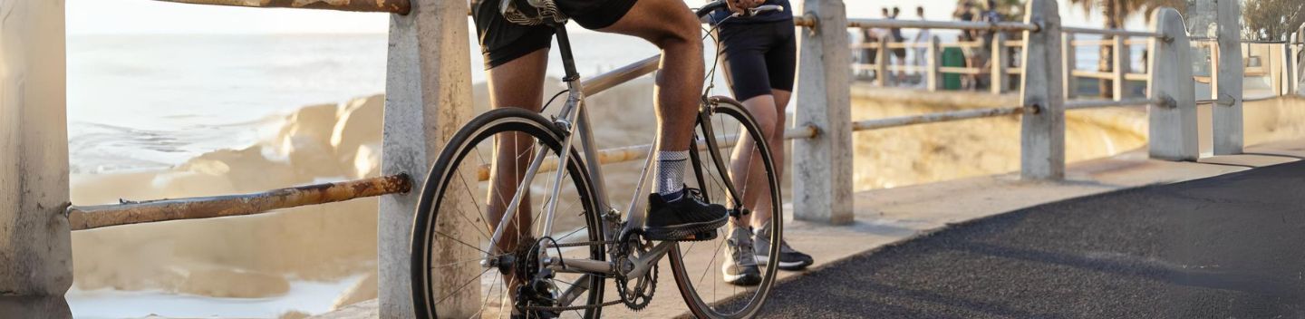 Man talking to his friend at the railing at Bondi Beach. The man is on a bicycle and wearing a Bauerfeind ankle brace to help manage ankle arthritis symptoms