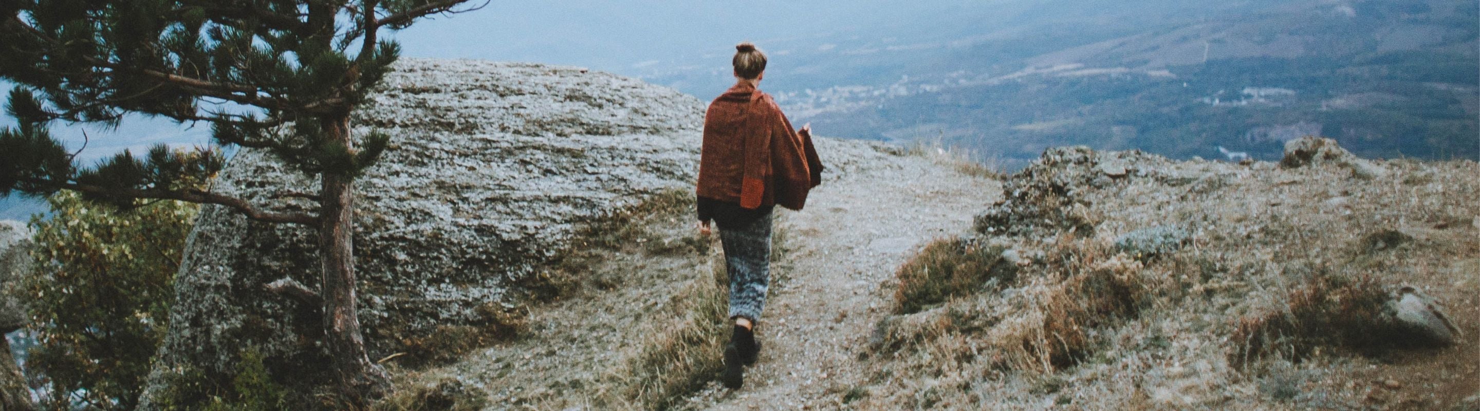 Woman in jeans and a shawl walking up a hill