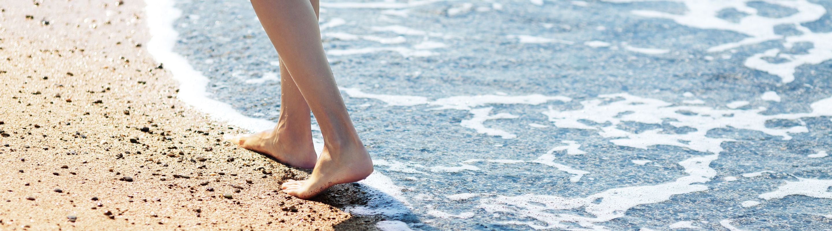 Person walking barefoot on the beach to improve their flat feet. They're wearing a yellow top and blue jeans.