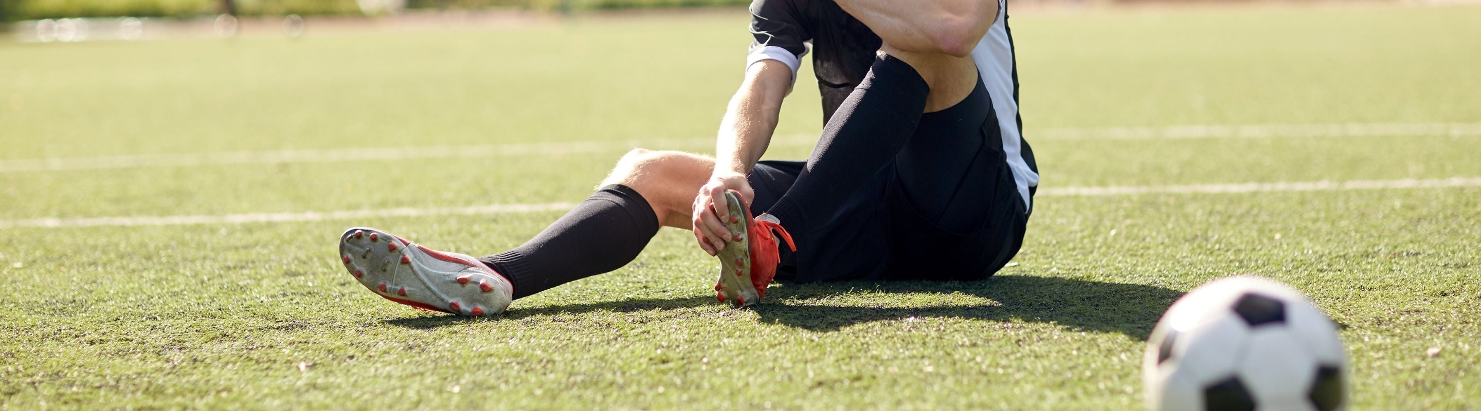 soccer player sitting down on the field holding his foot