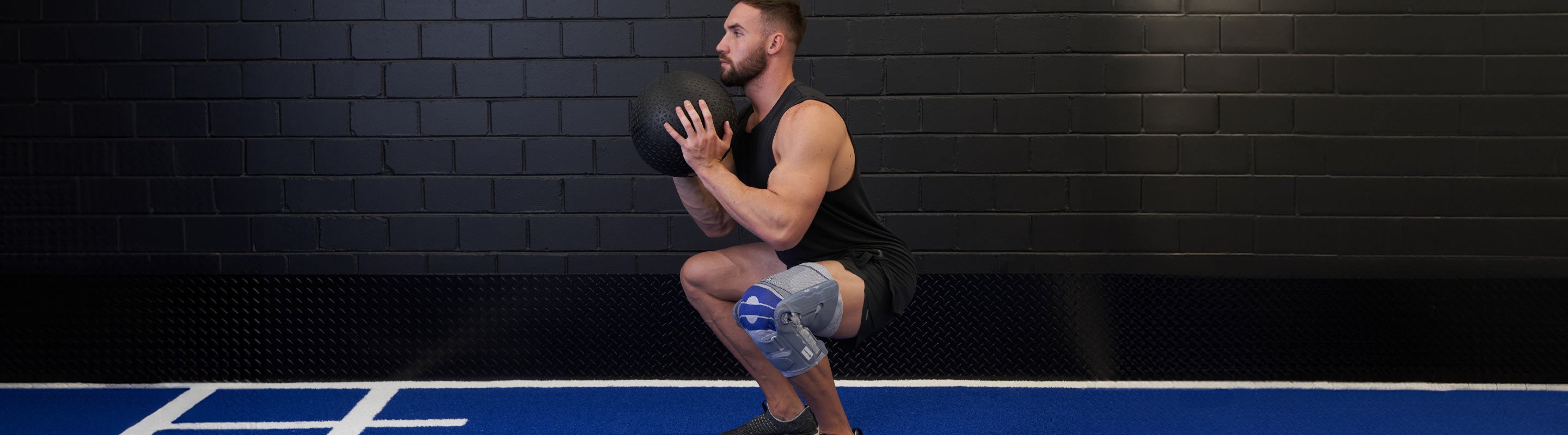 Man at the gym doing kettle bell squats. He is wearing Bauerfeind SofTec Genu to relieve knee pain