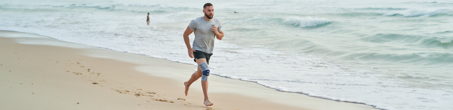 man running on the beach wearing a Bauerfeind GenuTrain Knee Brace to fight knee pain from running