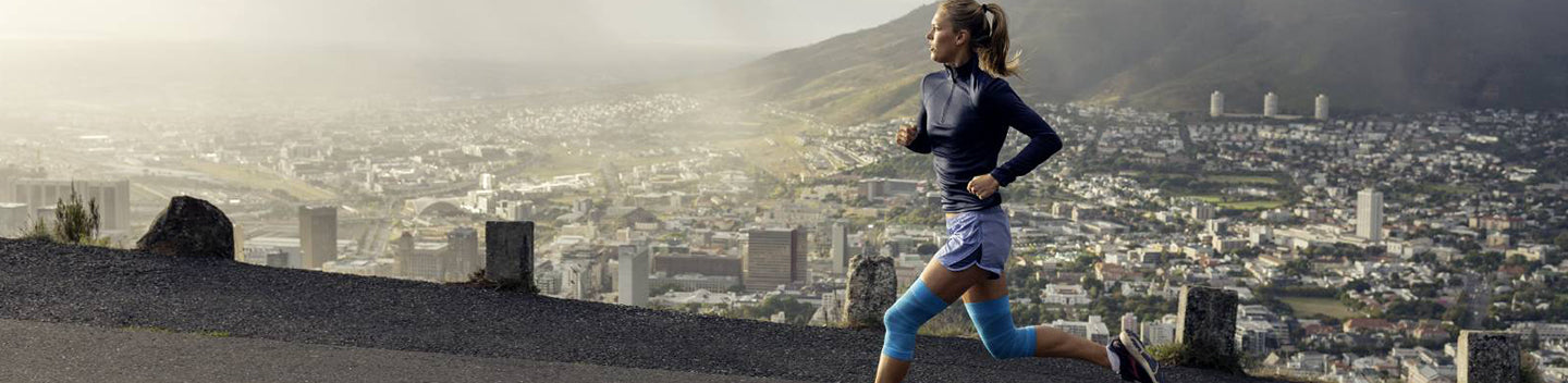 woman running up the road in knee compression sleeves, a good piece of running gear to help reduce muscle fatigue