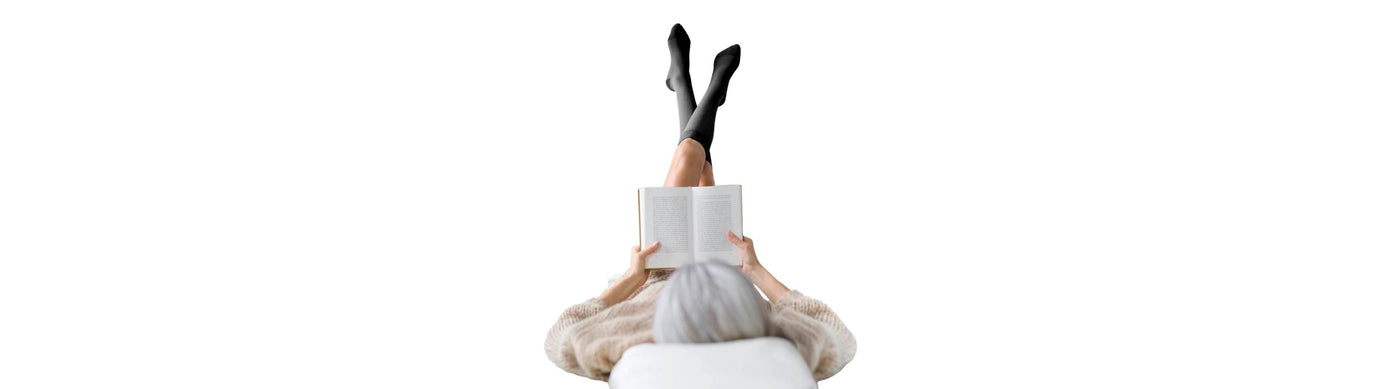 woman wearing Bauerfeind VenoTrain Cocoon Compression Socks while laying down reading with her legs in the air.