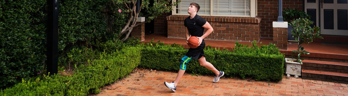 man practicing shooting for basketball. He is wearing Bauerfeind's Sports Knee Support