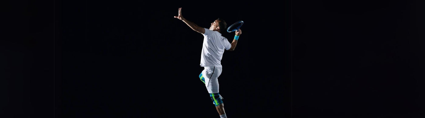 Man playing tennis. He is hitting backhand. He's wearing Bauerfeind's Sports Knee Suport