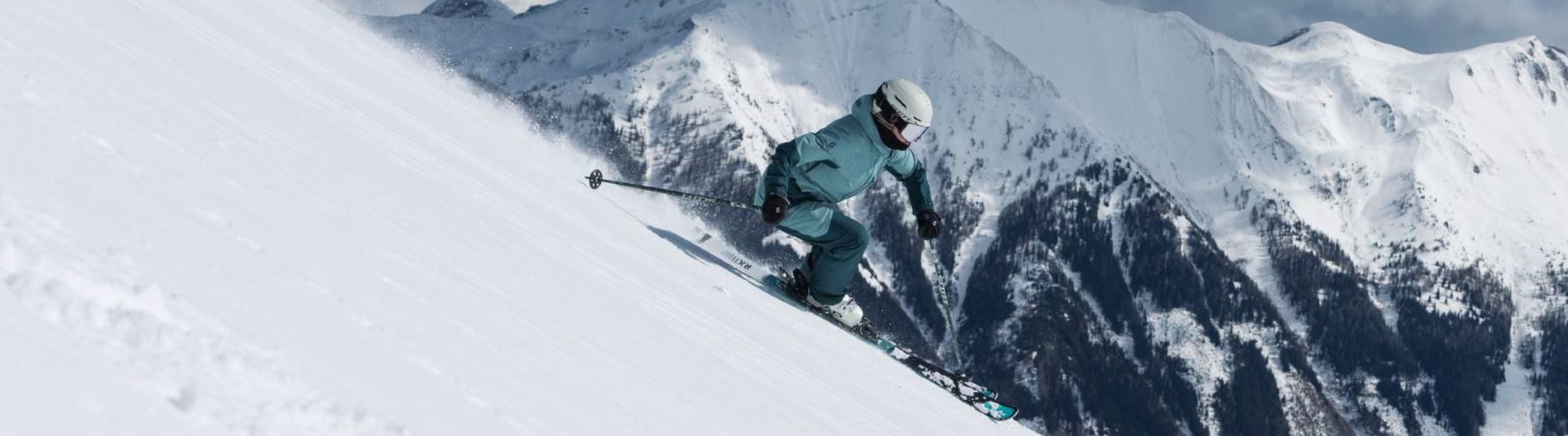 Pesron skiing down a slope with snowy mountain peaks in the background