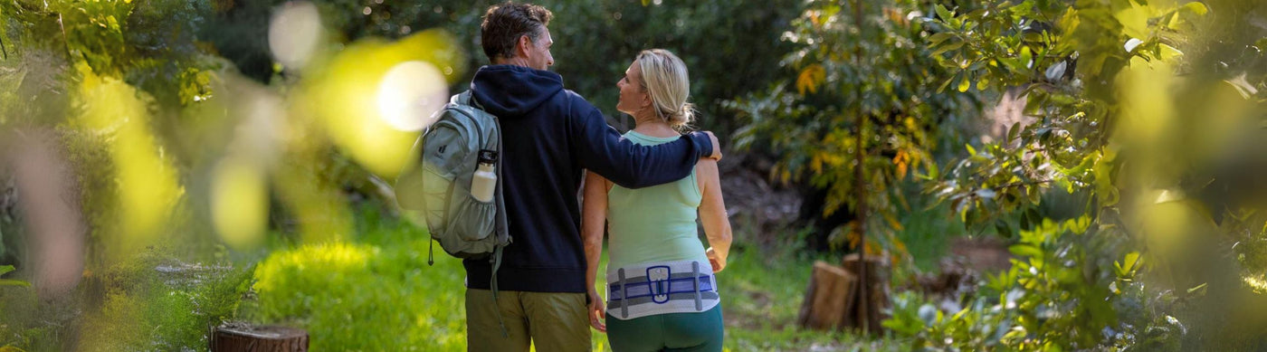 Man and woman out hiking. The man is side-hugging the woman and she is wearing Bauerfeind's SacroLoc Back Brace to manage back pain