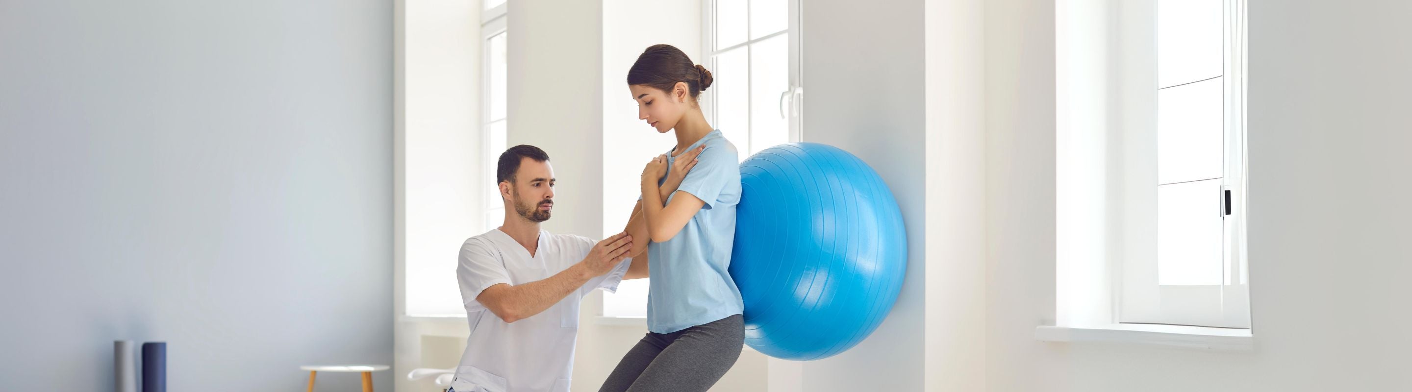 woman doing stability ball wall squats with the help of a physiotherapist