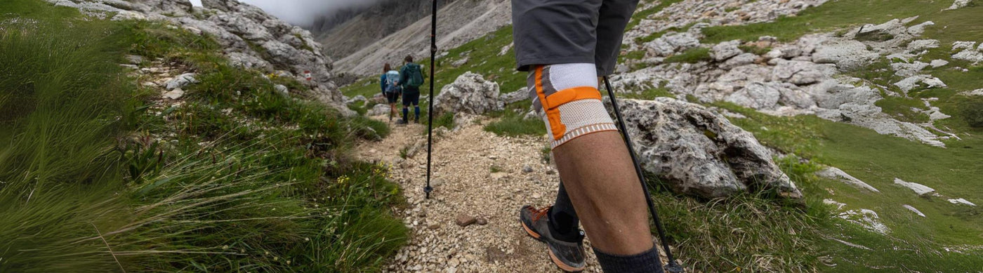 Person hiking through the mountains with the help of hiking sticks and Bauerfeind's Outdoor Knee Brace