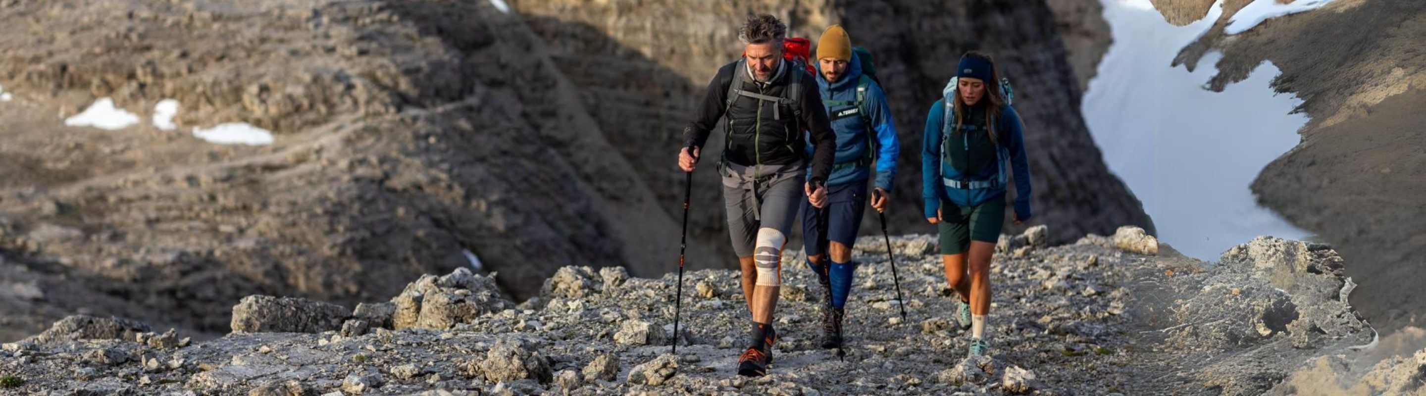 People hiking through snowy mountains. They are wearing compression supports, and the man out front is wearing a knee brace