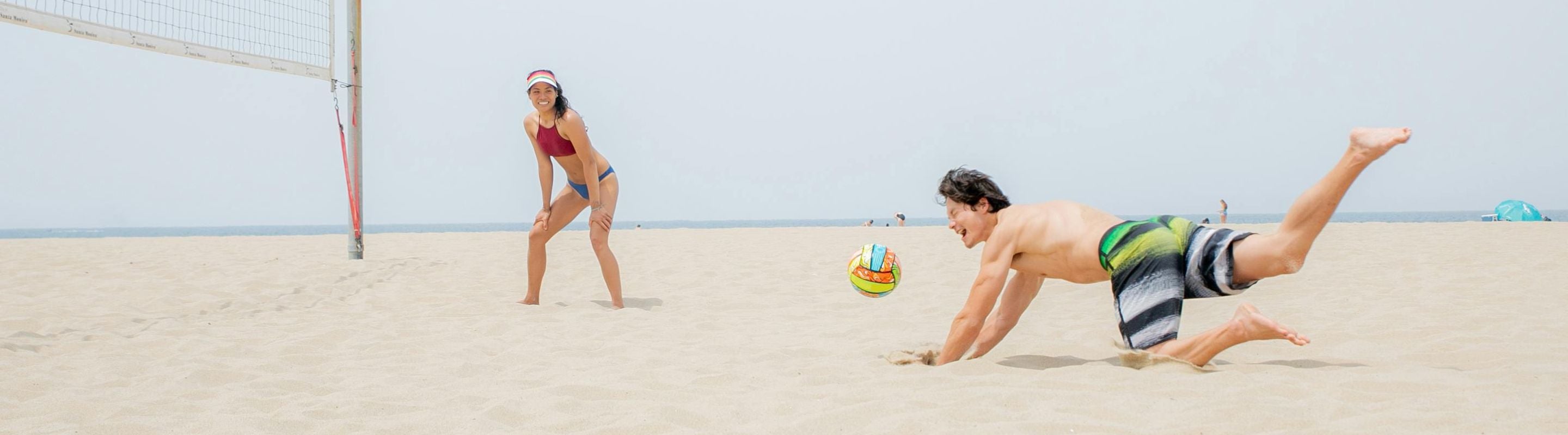 Young people playing beach volleyball. One of the players is falling in an attempt to catch the ball