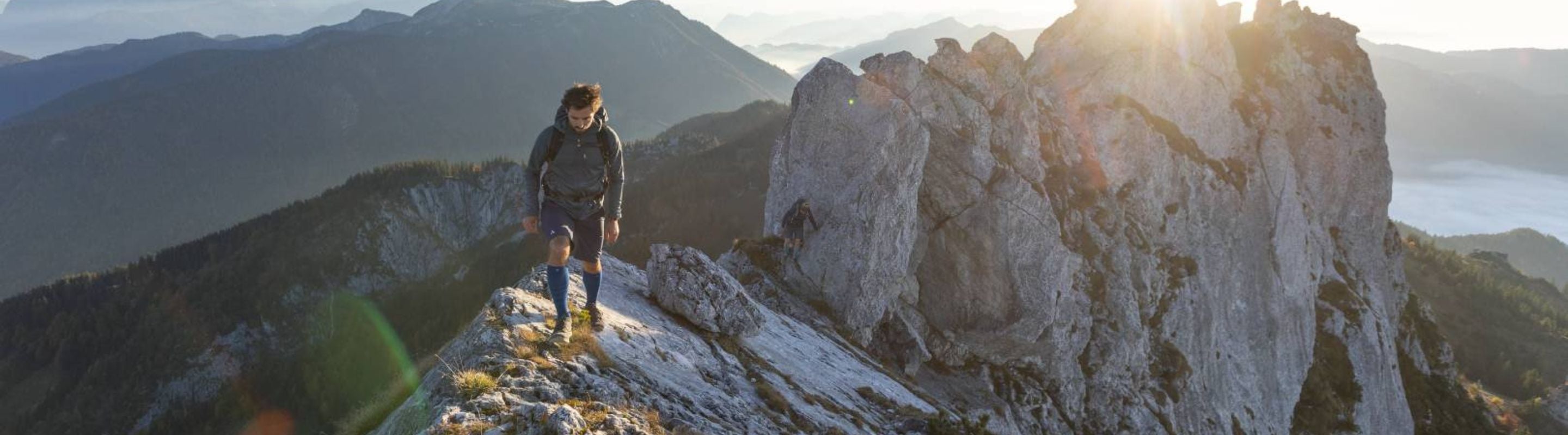 Man hiking across a rocky mountain range. Hi is wearing compression socks for hiking