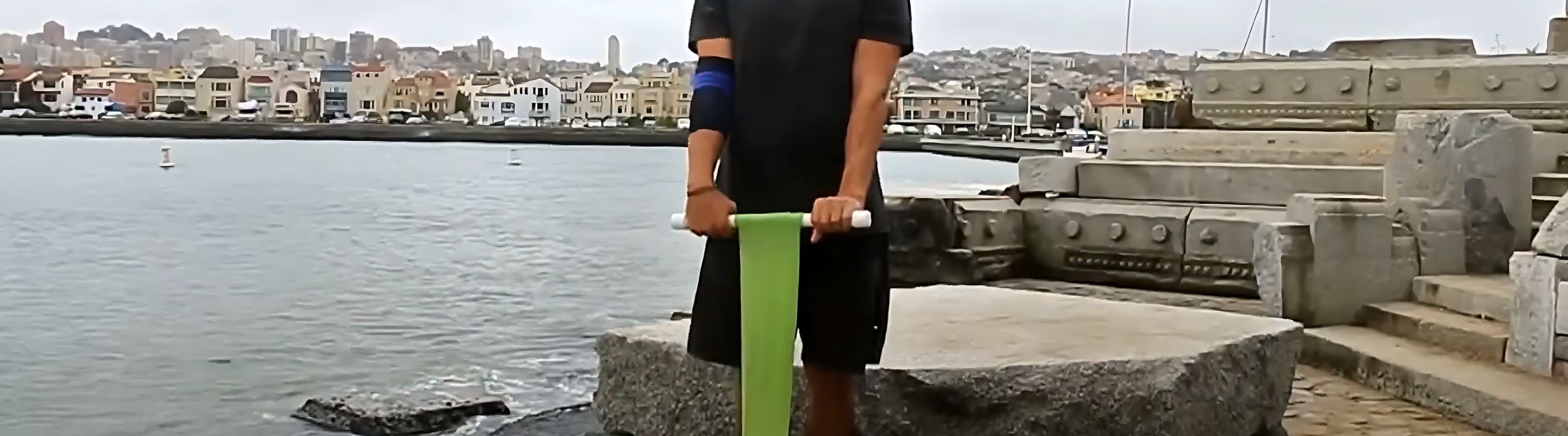 Man at the harbor performing the wrist roller extensions workout. He is wearing Bauerfeind's EpiTrain Elbow Brace for better support