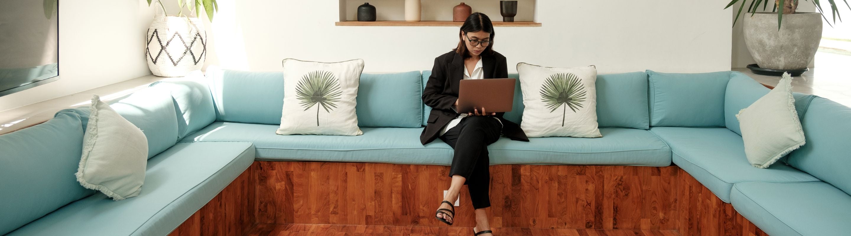 woman sitting on a window seat while working on her laptop, not an ideal set up for preventing back pain when working from home