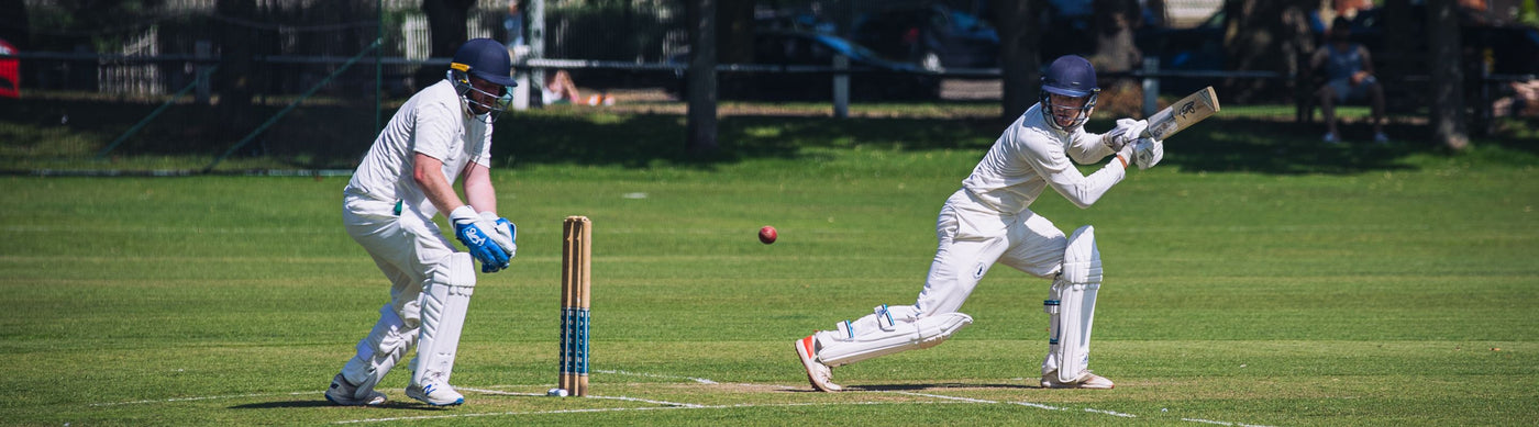 Two cricket players at the wickets. Once has missed the ball with his bat and the other is attempting to catch it