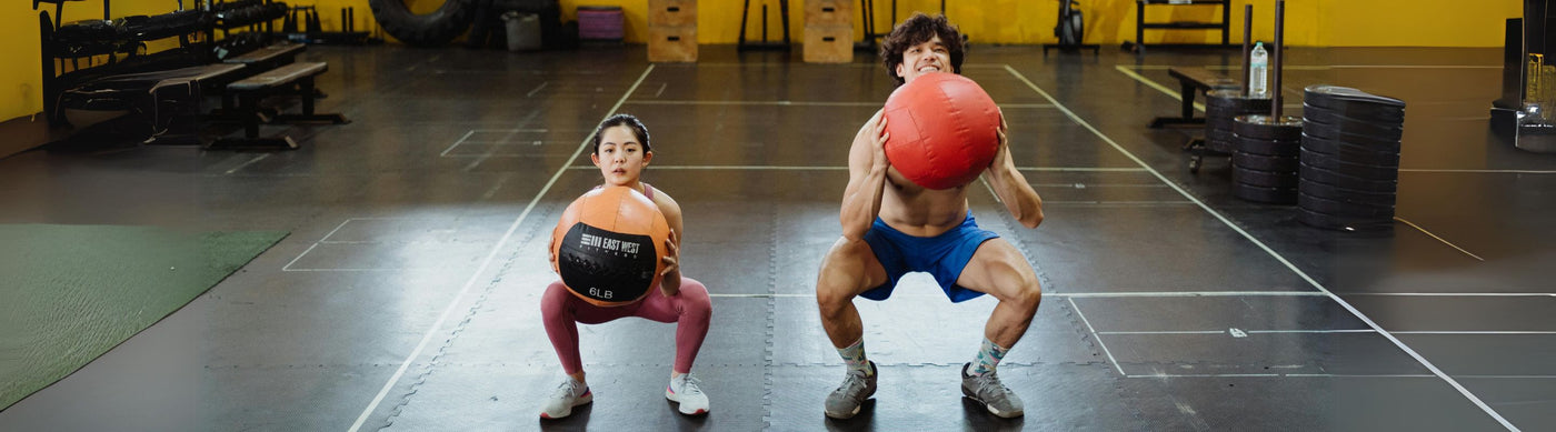 man and woman doing sump squats at the gym holding weighted gym balls