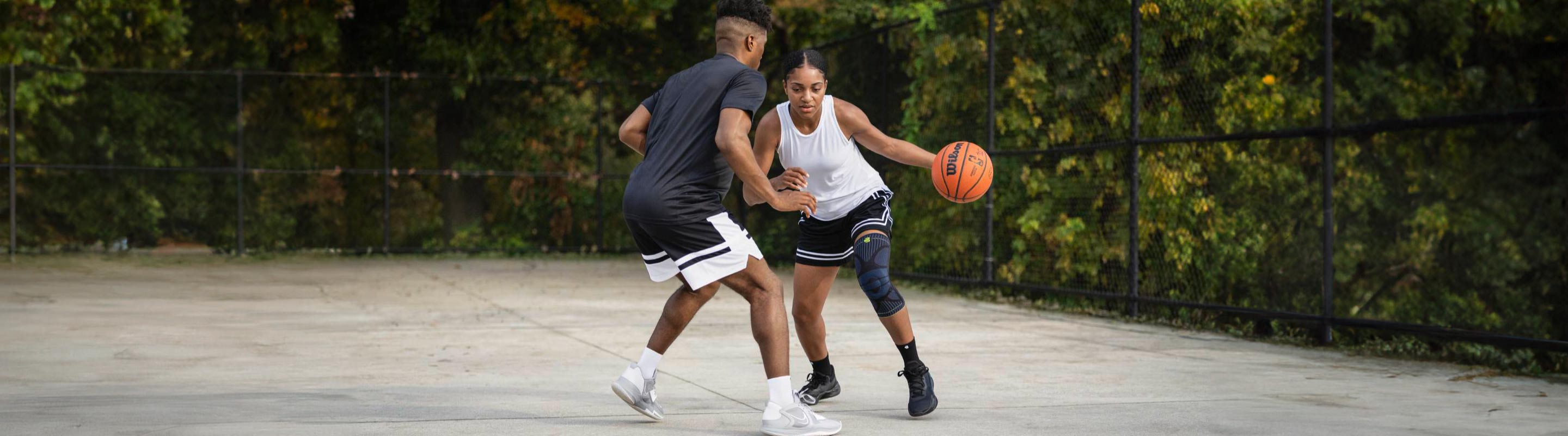 Basketball player in the middle of dribbling on an indoor basketball court. He is wearing a Bauerfeind Knee Compression Sleeve, a good way to avoid some of the most common injuries in basketball.