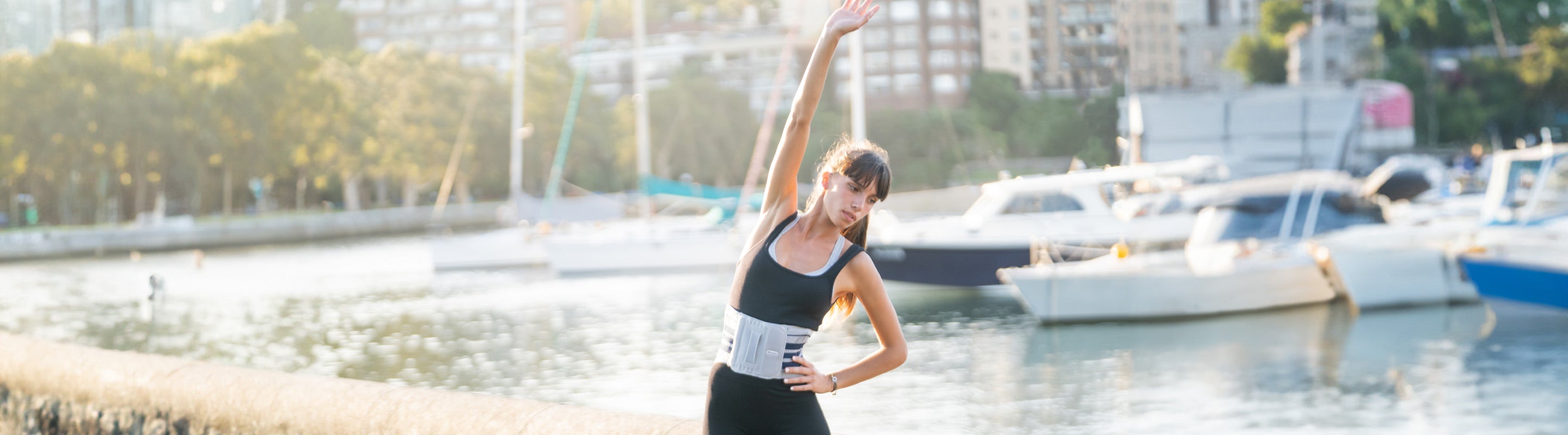 woman stretching her lats with an overhand reach. She is wearing Bauerfeind's LumboTrain Back Brace to relieve back pain