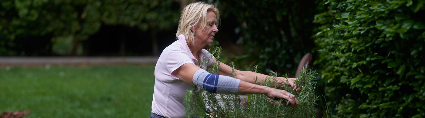 Older woman trimming plants with gardening shears. She is wearing the EpiTrain Elbow Brace to protect her elbow from gardening pain