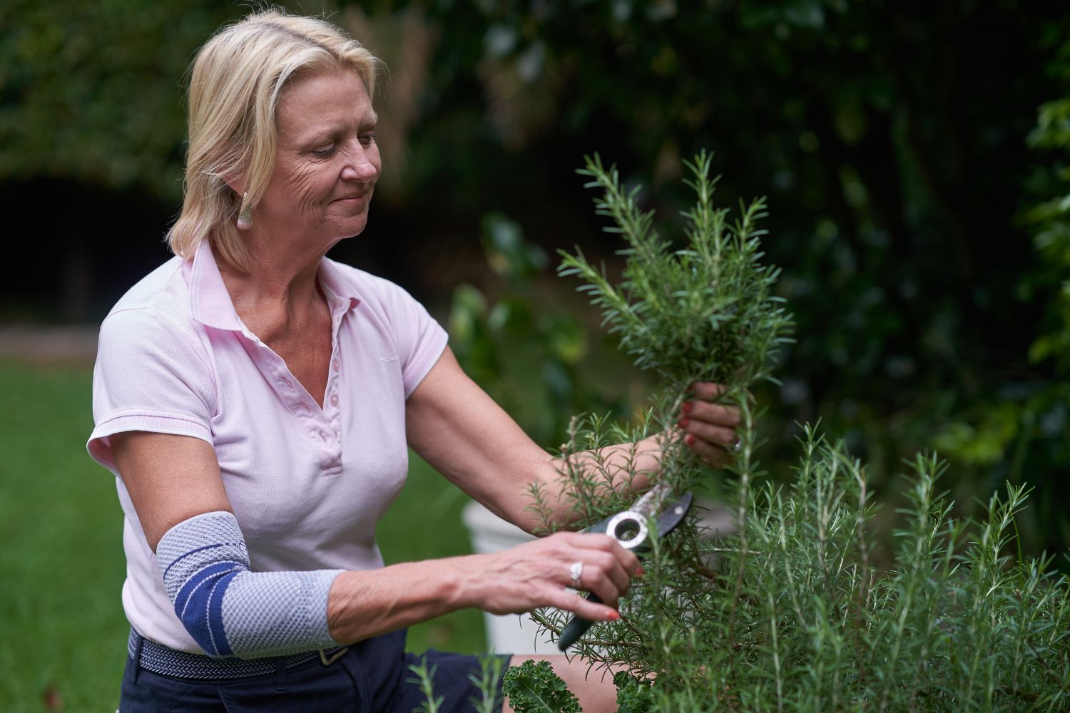 Older woman trimming plants with gardening shears. She is wearing the EpiTrain Elbow Brace to protect her elbow from gardening pain