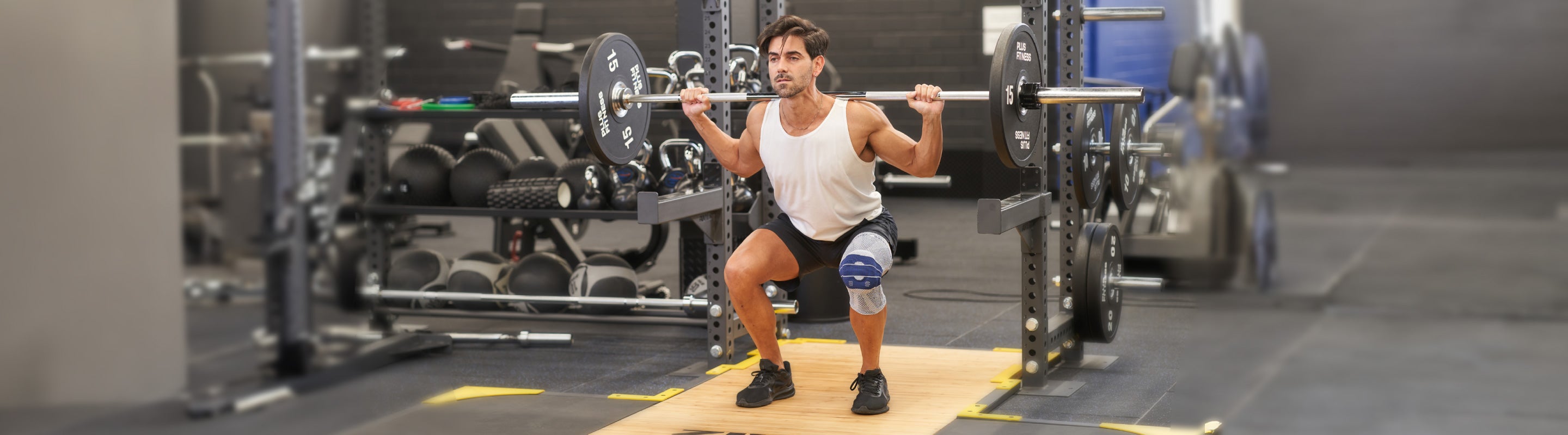 Man doing squats at the gym, He's reading a barbell with 2 15 kg weights on his shoulders. He's wearing Bauerfeind's LumboTrain back brace to support his spine through the squat.