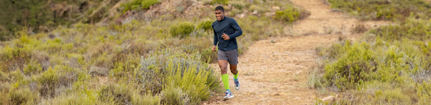 Man running in calf sleeves, a good way to avoid ITB Syndrome. He's running a long a lake on a semi-cloudy day