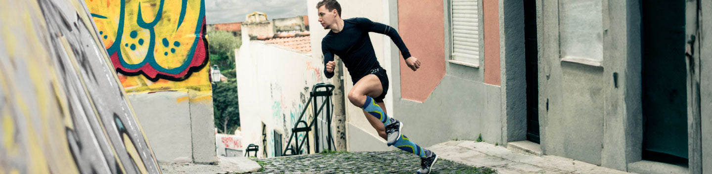 Wide shot of a triathlete in athletic gear and performance compression socks turning a corner as he's rinning down the street