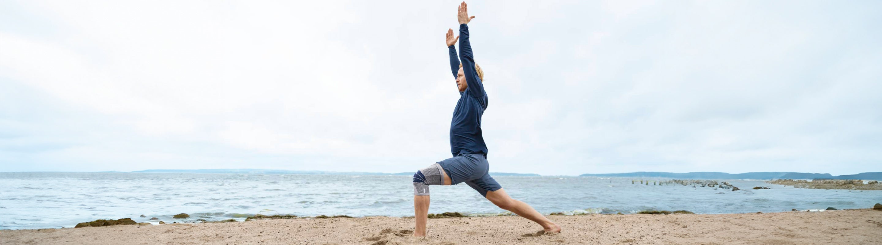 Man on the beach doing exercises for his knee pain. He is wearing Bauerfeind's GenuTrain Knee Brace for added support