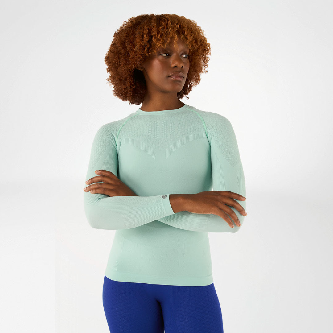 Woman wearing a light green Bauerfeind compression long-sleeve top and blue leggings on a white background