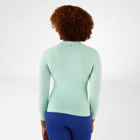 Person wearing a light green Bauerfeind compression long-sleeve top and blue pants on a white background