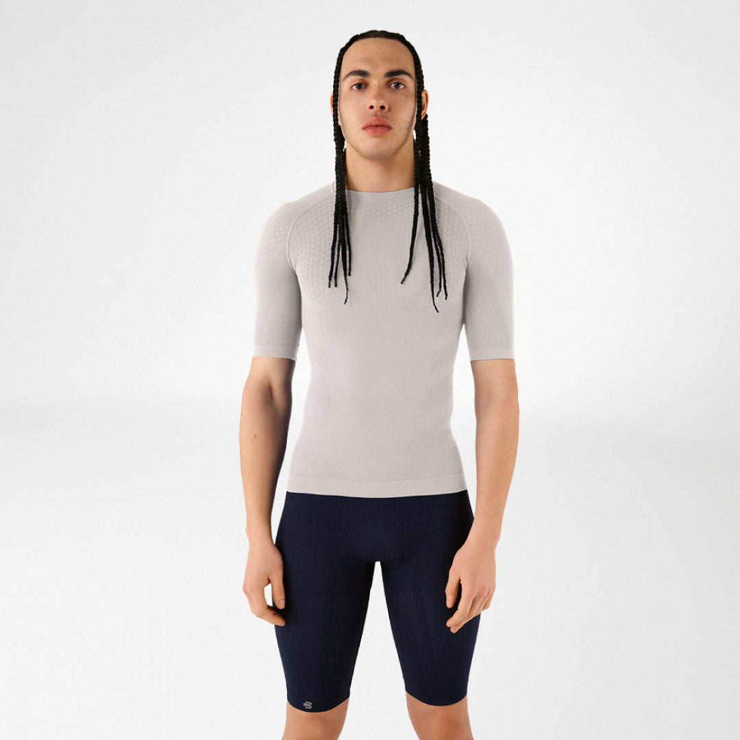 Person wearing a grey Bauerfeind compression short-sleeve top and navy shorts on a white background.