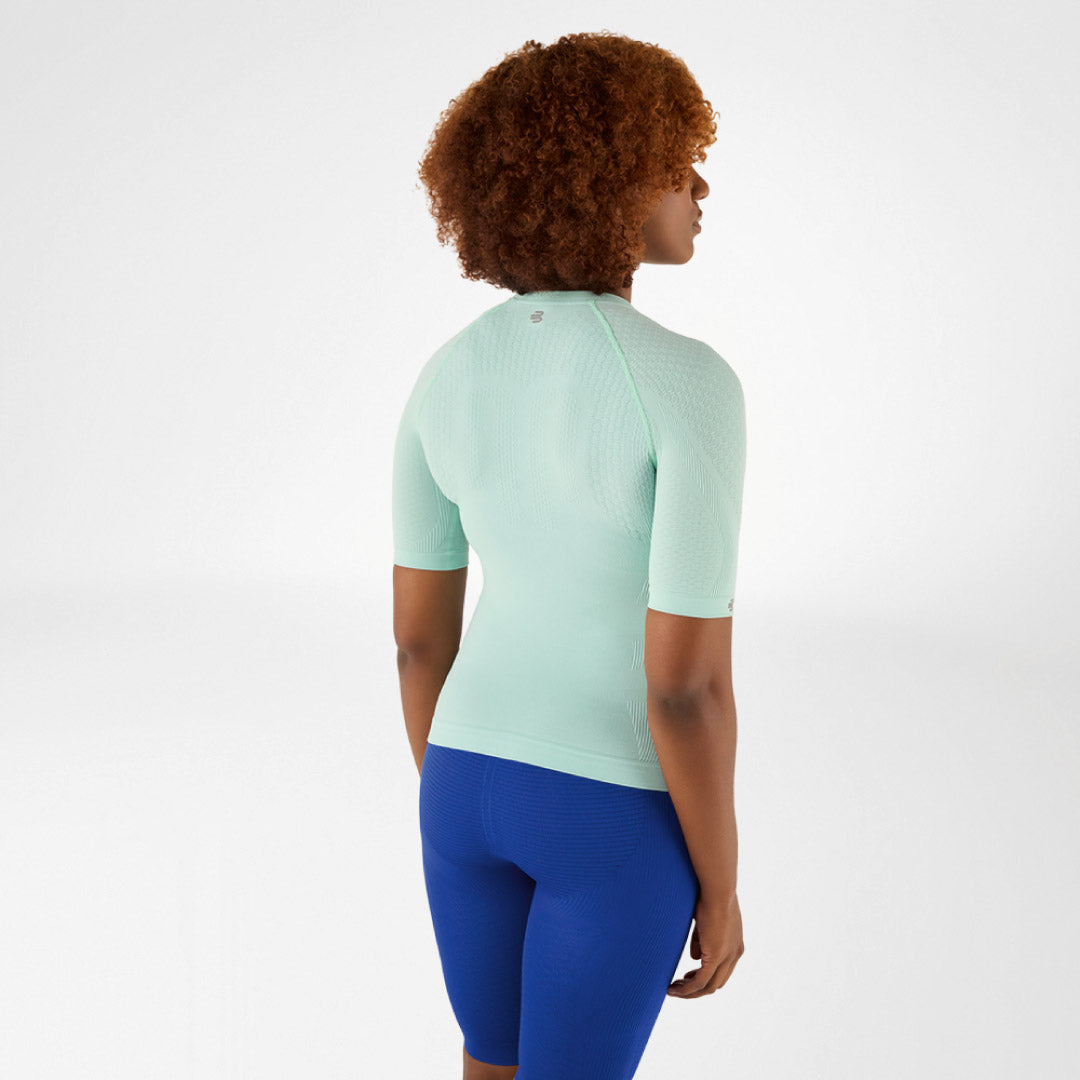 Person wearing a light green Bauerfeind compression shirt and blue leggings on a white background