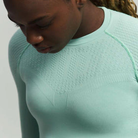 Person wearing a light green Bauerfeind compression shirt with a textured pattern on a plain background