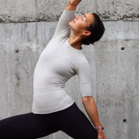 Person in a yoga pose against a concrete wall wearing a silver Bauerfeind compression shirt